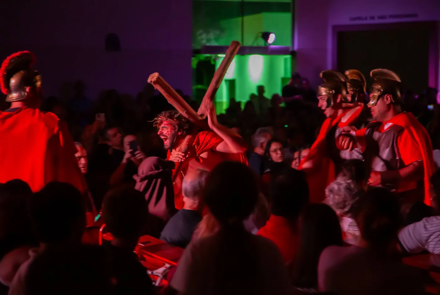 Christ carrying the cross through the crowd, red light against a green backdrop
